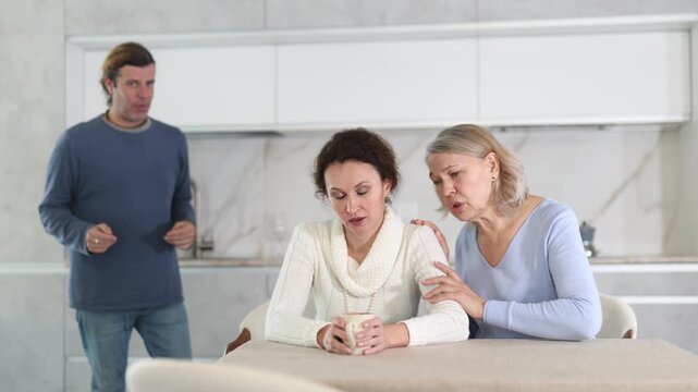 Woman sits near daughter and comforts during quarrel with husband. Mother calms upset daughter takes side of woman in altercation with adult brother. Man is outraged by girlfriend behavior and blames