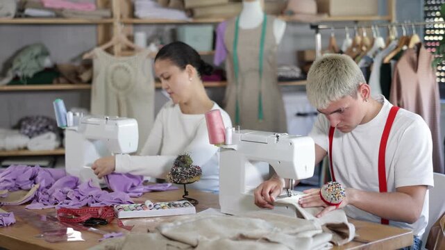 Tailors are working on a collection of clothes. Male tailor working in team with Asian female seamstresses, they sew the sample for approval with customer. High quality 4k footage