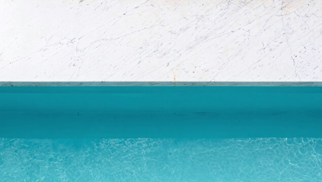 Top down view of white marble edge meeting turquoise blue swimming pool water