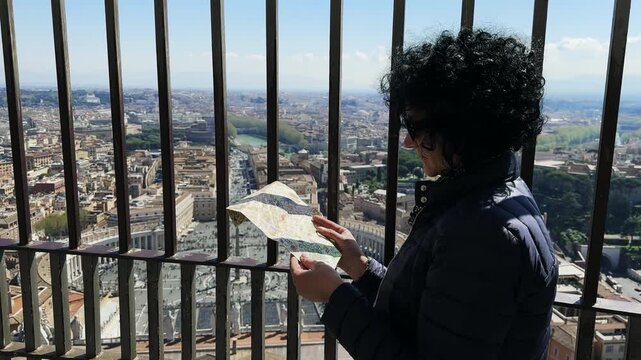 Visitor woman at Saint Peter church dome enjoy panoramic view of Rome looking for landmark locations on map, slow motion cinematic shot