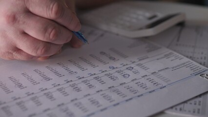 Person writes notes on paper while using a calculator at a desk to manage financial information during a work session in an office environment