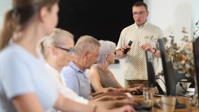 Enthusiastic male tutor teaching group of seniors in computer workshop, promoting technology adoption among older generations