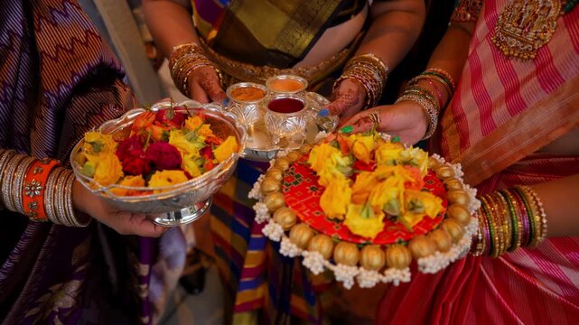 Women holding traditional offering plates with flowers and ceremonial items during Indian wedding ritual. Close up of cultural preparation in colorful ethnic attire.