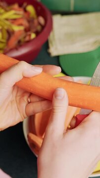 Vertical close-up of woman&rsquo;s hands slicing a carrot with a kitchen knife, trimming veggie sticks for meal prep on countertop, home cooking b-roll.