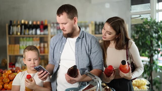Pleased couple and their little boy checking QR code on bottle of juice in supermarket 