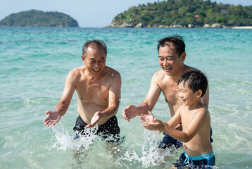 Fototapeta premium Three Generations of Thai Men Splashing in Ocean Waves