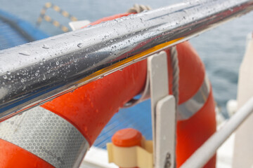 Wet Metal Handrail and Orange Lifebuoy on Ship Deck with Raindrops