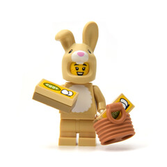 Fototapeta premium Lego minifigure of happy bunny is hunting easter eggs isolated on white. Editorial illustrative image of Easter holiday by popular plastic bricks constructor.