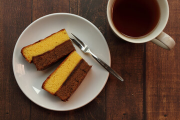 Chocolate and vanilla layered sponge cake on white plate and a glass of tea.