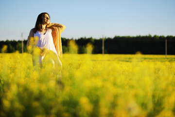 Fototapeta premium Pretty girl with a hat in her hand walks in a field with field flowers and smiles sincerely