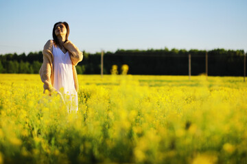 Fototapeta premium Pretty girl with a hat in her hand walks in a field with field flowers and smiles sincerely