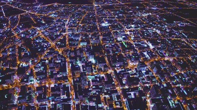 aerial night urban grid seen from drone showing illuminated streets, rectangular blocks, amber streetlights, cool blue window glows, sparse traffic, calm suburban geometry for planning and mapping
