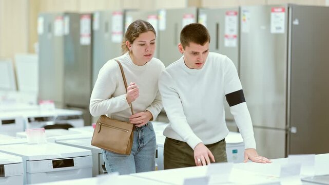 Couple after repairing their apartment came to a home appliance store and chooses a dishwasher and a washing machine. Man and a woman choose household appliances. High quality 4k footage