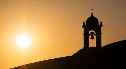 Silhouette of a church bell tower with a cross against a golden sunset sky