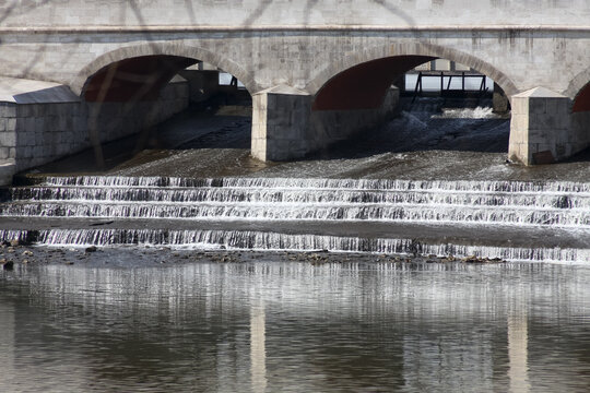 Urban drainage cascade with stepped weir. Excess stormwater flows from upper pond to lower basin creating small waterfalls under bridge