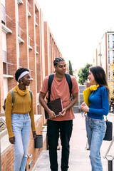 Obraz premium Multiracial young students carrying notebooks and backpacks, talking and walking on campus, embracing friendship and education