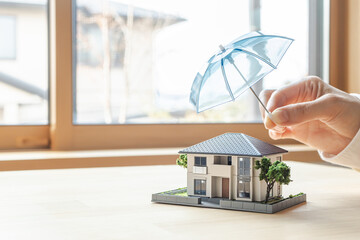  傘で安全に守られる家の模型　住宅の火災保険や地震保険　家のセキュリティ