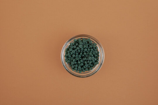 Secondary polypropylene granules green color in glass bowl, top view. PP granules. Recycled polymer made from post-consumer or post-industrial plastic waste. Zero waste