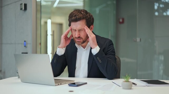 Professional business experiences a debilitating headache while intensely working at office, gripping temples in discomfort. Feeling overwhelmed and exhausted.