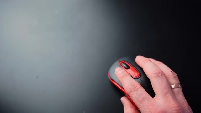 Top-down close-up of a hand resting on a black and red wireless mouse on a clean dark desk with large copy space, ideal for office productivity, UI navigation, and tech b-roll.