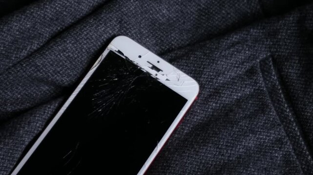 Broken cracked smartphone screen Phone red on dark fabric background, shattered glass display damage concept
