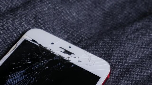 Broken cracked smartphone screen Phone red on dark fabric background, shattered glass display damage concept