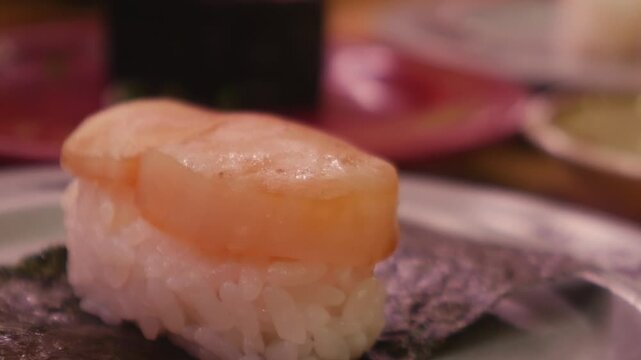 Seared scallop nigiri sushi with nori on decorative plate at Japanese restaurant, golden glazed shellfish