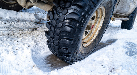 Offroad tire on snowy road with winter traction. Close up of all terrain wheel in snow. Rugged SUV tire driving on snow. Car tire close up on icy winter road. Off road tire with deep tread on icy road © Volodymyr