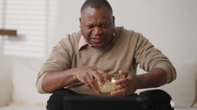 Mature man watching scary movie in evening and fearing, throwing popcorn up. Shock and fear, horror movie, emotional captured spectator sitting alone in living room, lazy day in weekend at home
