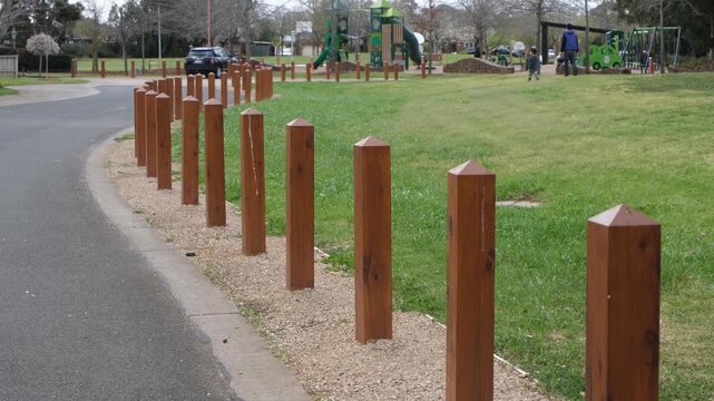 Timber bollards separating a green open area from a road in a suburban park in Australia, with a children&rsquo;s playground, people in distance. Protective buffer enhance safety in family-friendly zone