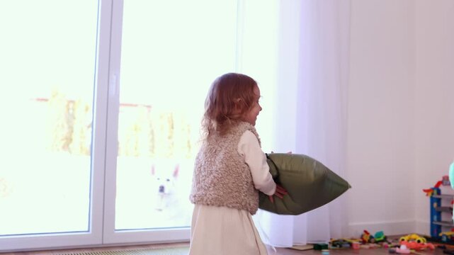 A little girl with curly hair carries a large green foil balloon in the shape of a star. She moves through a sunlit room, enjoying a moment of indoor play
