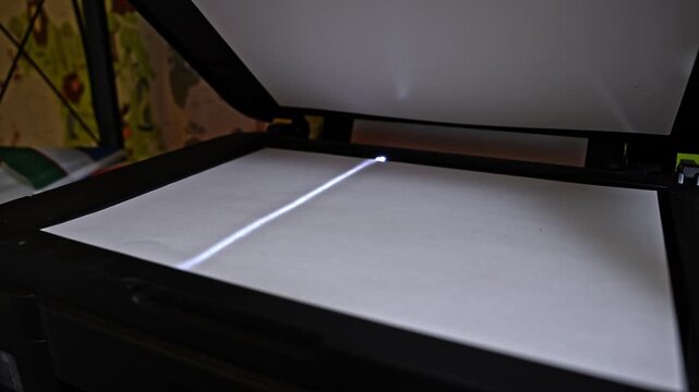 Closeup view of flatbed scanner slowly scanning paper document. Optical device moving light bar during office digitization process.