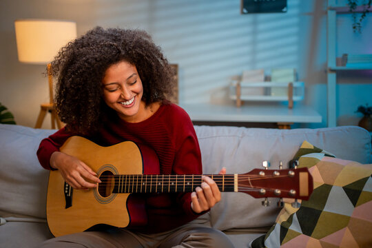 Latina beautiful woman playing guitar in living room at home. 