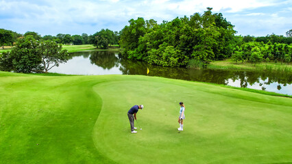 Drone view of young golfers swing clubs together on a scenic golf course. © Kawee