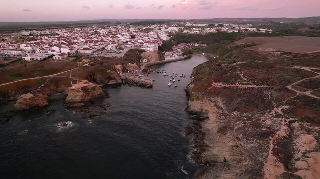 Porto Covo village overlooks fishing harbor carved into rocky Atlantic coastline within Costa Vicentina Natural Park in Alentejo region Portugal featuring dramatic cliff formations with tipical homes