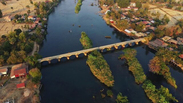 Aerial view of the historic French colonial bridge connecting Don Det and Don Khon islands over the Mekong River in southern Laos, surrounded by lush vegetation and village houses.