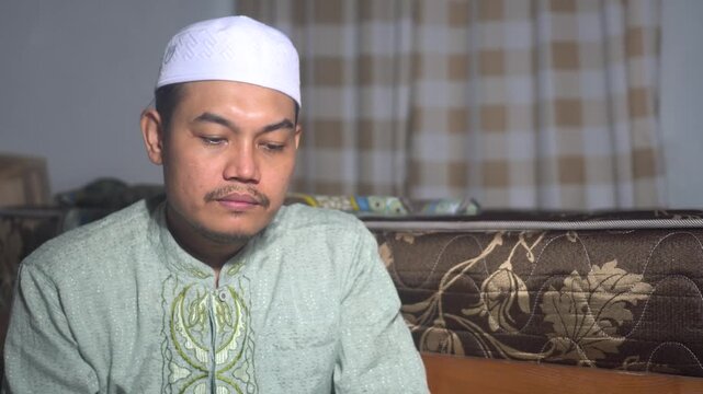 Pious Asian Muslim man in traditional dress and songkok cap using an incense burner (mabkhara) at home. Serene atmosphere for prayer preparation, Islamic lifestyle, and religious rituals during Ramada