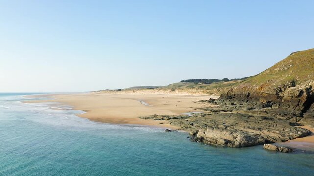 Wide sandy beach with rocky outcrops and clear blue water at Plage de la Vieille eglise, France, under a clear sky.