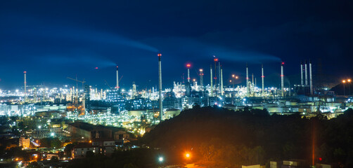 Fototapeta premium Large industrial petrochemical zone - oil refinery plant illuminates the night sky with glowing industry lights during oil production. 