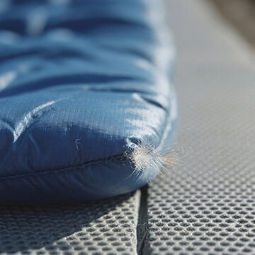 Gros plan sur l'extr&eacute;mit&eacute; d'une doudoune ou d'un sac de couchage bleu avec du duvet qui s'&eacute;chappe d'une couture