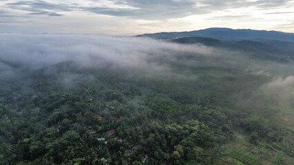 Aerial drone view of countryside with surrounding farmland and morning mist above with mountains and hills as background in the morning