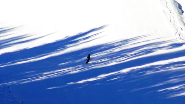 A lone skier glides down a sunlit ski slope in Megeve, France, with dramatic blue shadows cast by nearby trees across the pristine snow. Tranquil winter landscape in the French Alps.