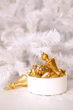 A set of gold glass Christmas tree ornaments in a round box against a white Christmas tree background. Single-color New Year's decor. 