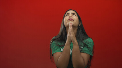 Woman volunteer wearing green t shirt presses hands together in prayer, eyes upturned and tearful...