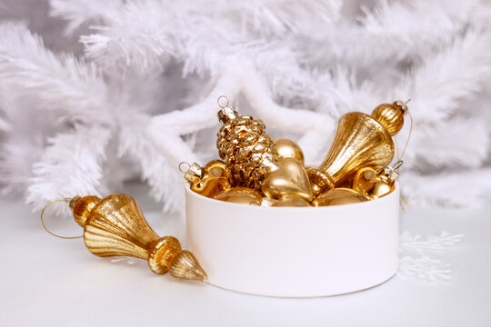 A set of gold glass Christmas tree ornaments in a round box against a white Christmas tree background. Single-color New Year's decor. 