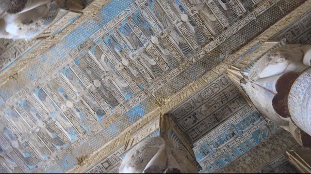 Looking up inside ancient Hathor Temple at Dendera, Egypt. Painted blue ceiling with gods and hieroglyphs between massive stone columns. Rare authentic temple footage. Downscaled from 6k.