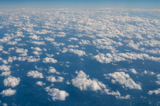 Looking down on fluffy clouds in blue sky from airplane window.