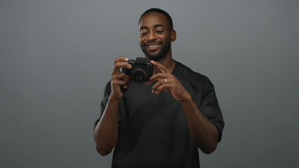Man holding dslr camera, smiling and adjusting lens with gold chain visible in gray studio  confidence creativity inspiration. © Krakenimages.com