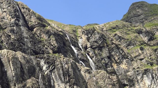Multiple waterfalls cascade down steep rocky cliffs under a clear blue sky in the Cirque de Gavarnie, French Pyrenees.