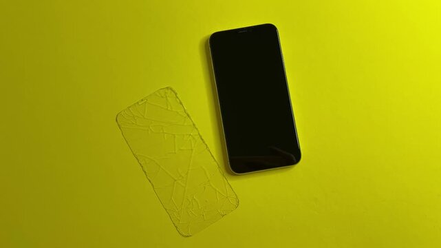 A removed protective glass next to an undamaged smartphone on mono bright background